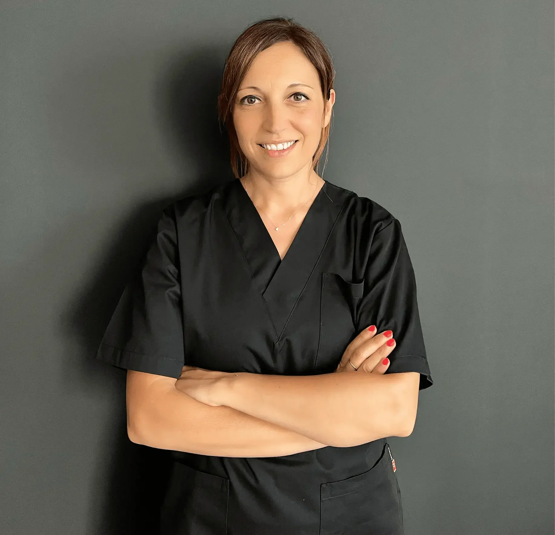 Ritratto di Marta, terapista specializzata in linfodrenaggio a Seregno, con camice nero e braccia conserte davanti a sfondo grigio.
